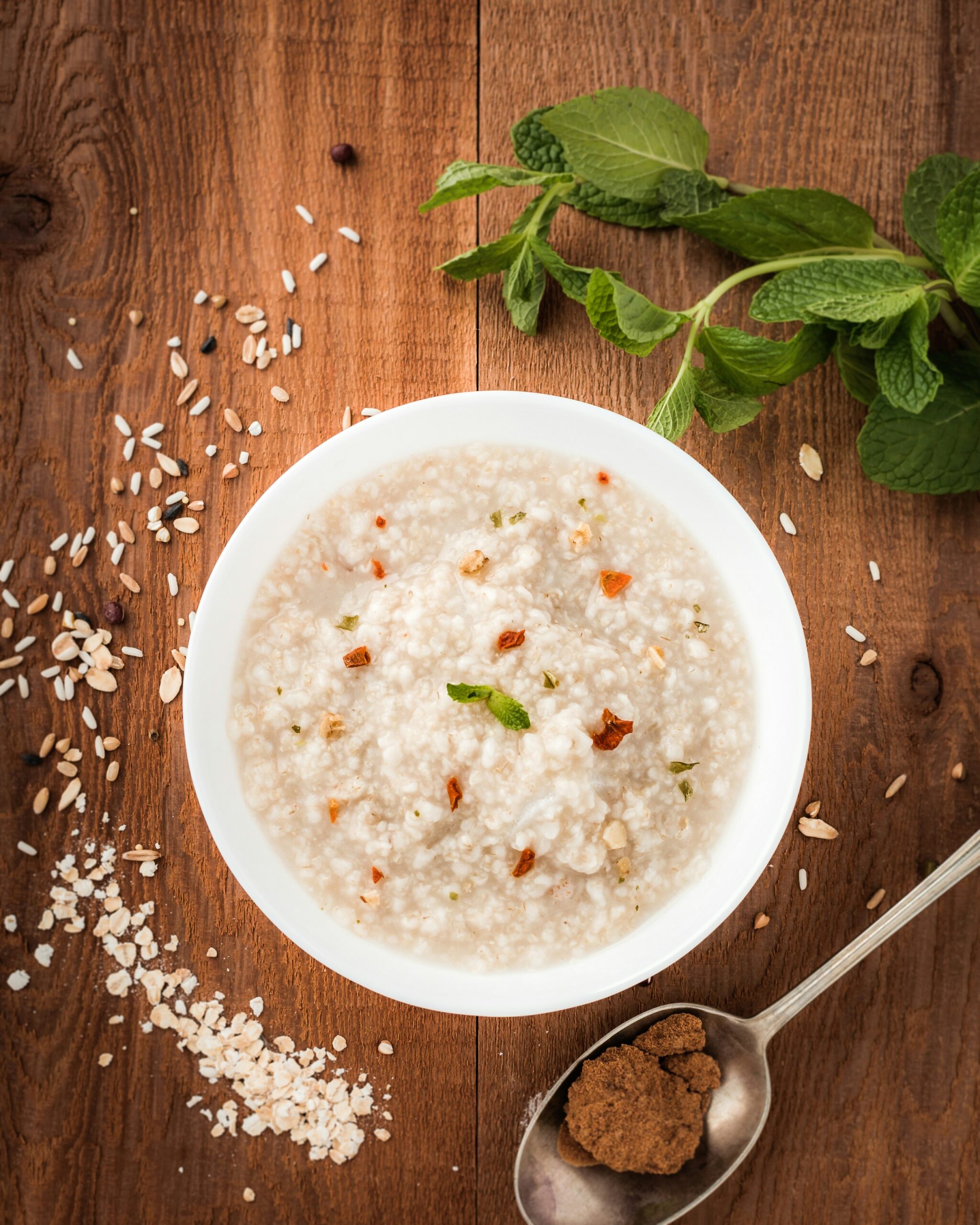 A warm bowl of congee garnished with herbs and seeds on a wooden table, symbolizing nourishment and gentle digestion in Traditional Chinese Medicine.